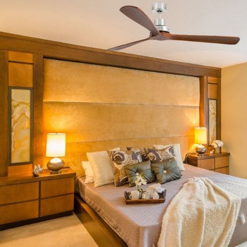 Ventilateur de plafond au-dessus d'un lit dans une chambre chaleureuse, avec lit élégant, chevets lumineux et décor apaisant. Avantages d'installer des ventilateurs de plafond dans chambres.