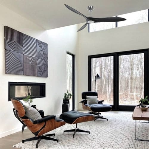 Salon moderne avec fauteuils Eames et ottomane, grande baie vitrée et ventilateur au plafond, ambiance lumineuse et cosy. clim et ventilateur en même temps pour optimiser la climatisation.