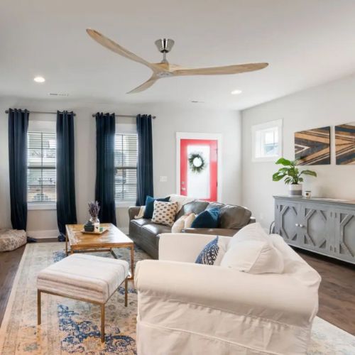Salon lumineux avec canapé, fauteuils et table basse sous un ventilateur au plafond.