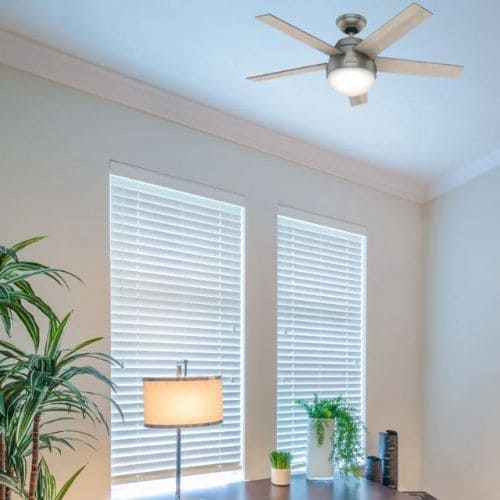 Ventilateur de plafond avec lumière fixé au plafond au milieu d’une pièce, ventilateur à quatre pales et abat-jour lumineux.